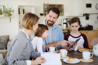 Eine Mutter und ein Vater sind mit ihren beiden Kindern am Frühstücken und diskutieren gemeinsam über das Taschengeld.